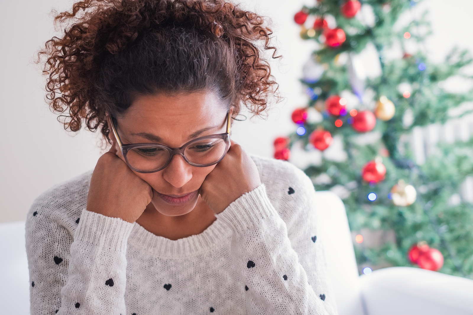 Sad woman sitting in front of Christmas tree, contemplating