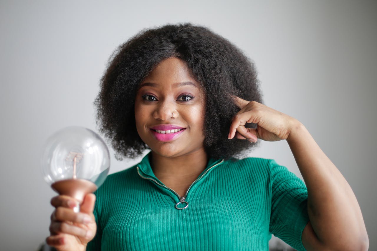 black woman pointing to her head and holding a light bulb