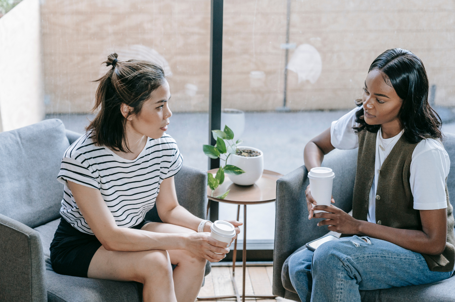 two women in conversation holding coffee cups