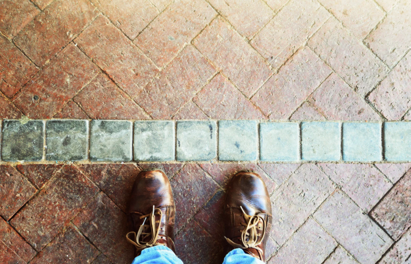 man stands with shoes up against green line of tiles in the floor