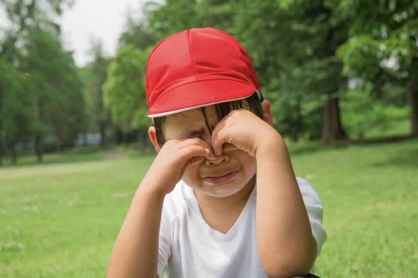 young boy in a red cap about to cry with hands over his eyes