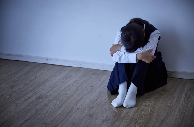 young girl sitting on the floor with head between her knees