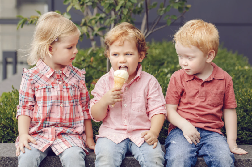 two children watch a boy sitting between them eat an ice cream cone