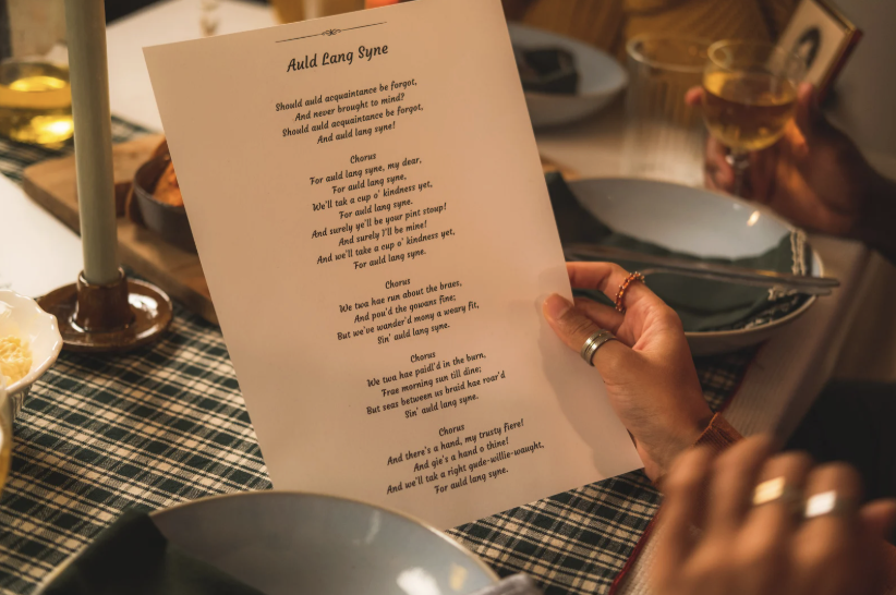 person holding paper with auld lang syne lyrics